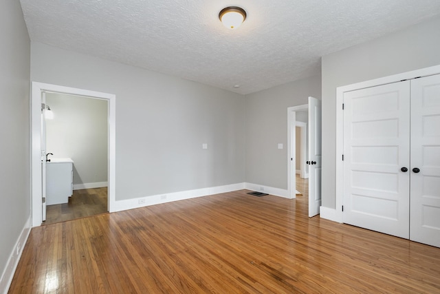 unfurnished bedroom with a textured ceiling, wood finished floors, visible vents, baseboards, and a closet