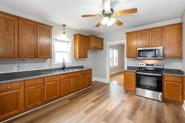 kitchen featuring stainless steel appliances, a sink, light wood finished floors, brown cabinetry, and dark stone countertops