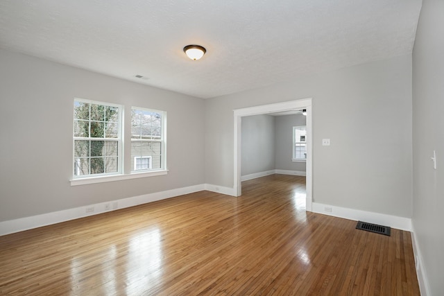 unfurnished room with a textured ceiling, wood finished floors, visible vents, and baseboards