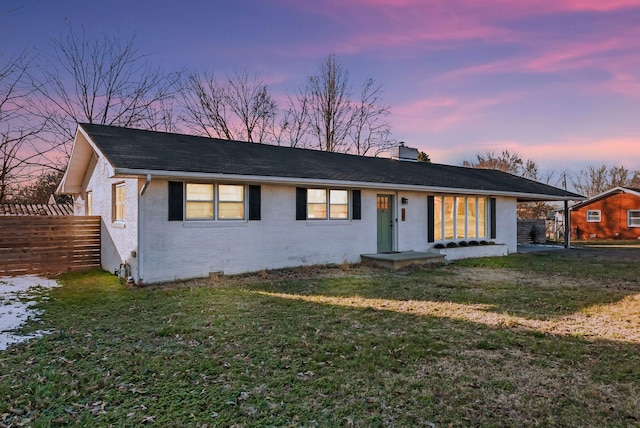 view of front facade featuring brick siding, a chimney, a lawn, fence, and a carport