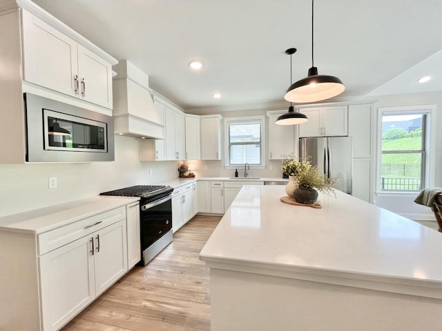 kitchen featuring custom range hood, hanging light fixtures, appliances with stainless steel finishes, white cabinets, and a sink