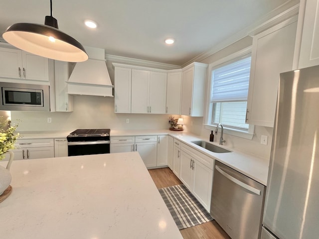 kitchen featuring custom range hood, decorative light fixtures, stainless steel appliances, white cabinetry, and a sink