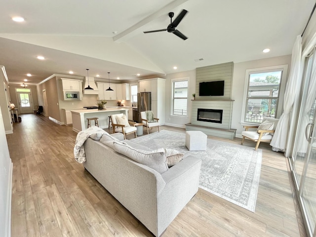 living area with vaulted ceiling with beams, a large fireplace, light wood-style flooring, and baseboards