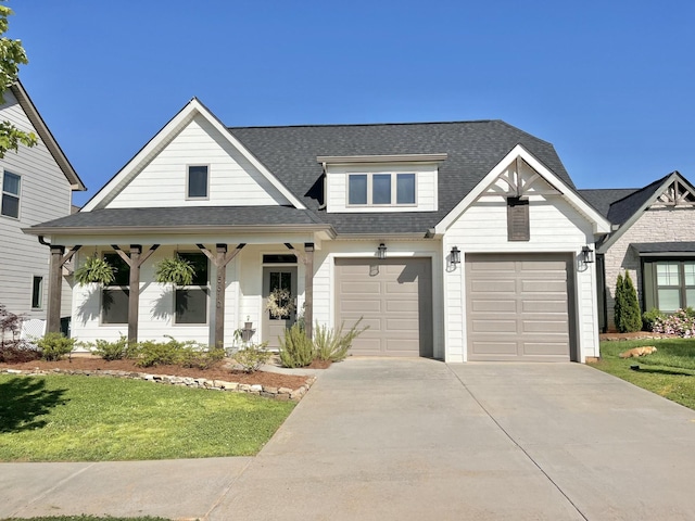 view of front of property with a garage, covered porch, concrete driveway, roof with shingles, and a front yard