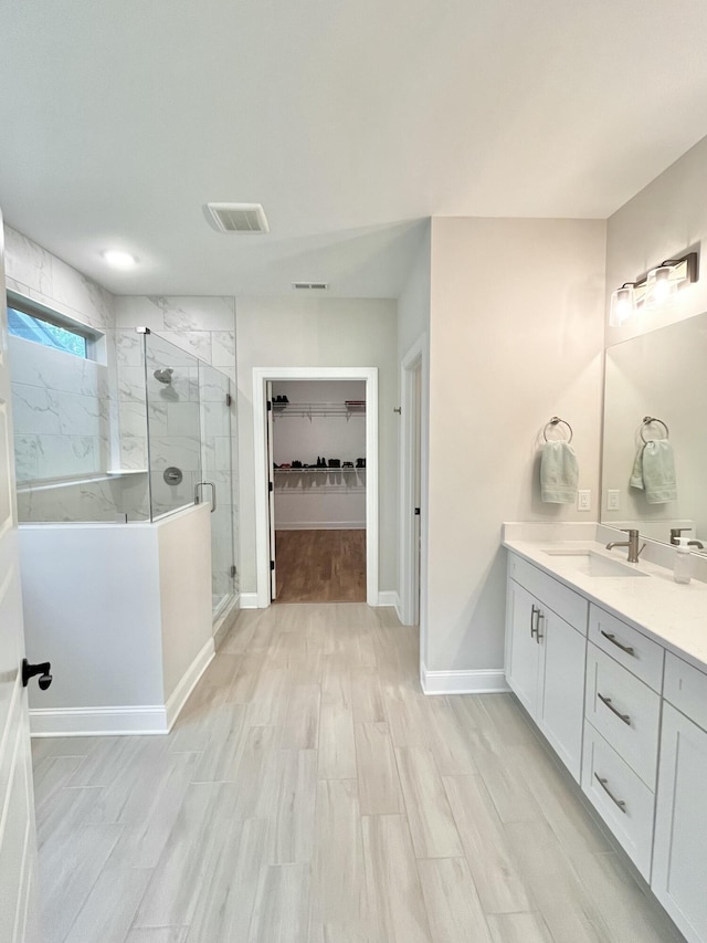 full bathroom featuring a marble finish shower, visible vents, vanity, wood finished floors, and baseboards