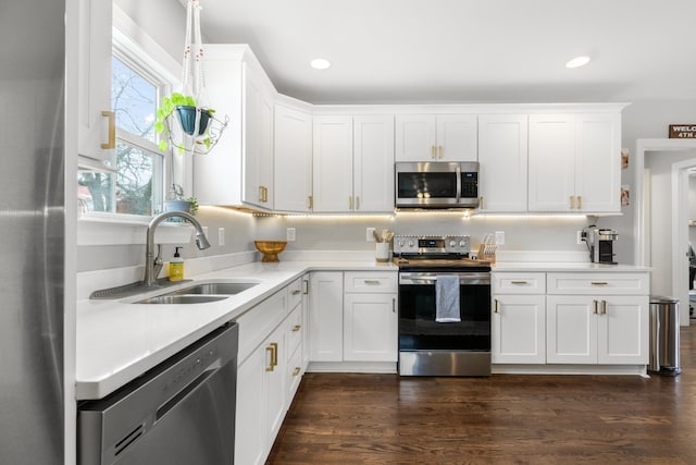 kitchen featuring stainless steel appliances, dark wood-style flooring, a sink, white cabinetry, and light countertops