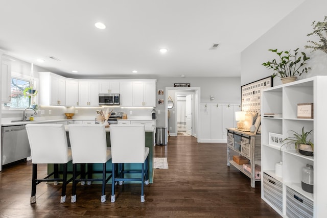 kitchen with a kitchen island, a breakfast bar, stainless steel appliances, light countertops, and white cabinetry