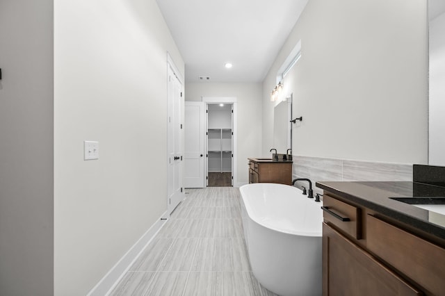 full bath featuring a walk in closet, a freestanding tub, vanity, and baseboards