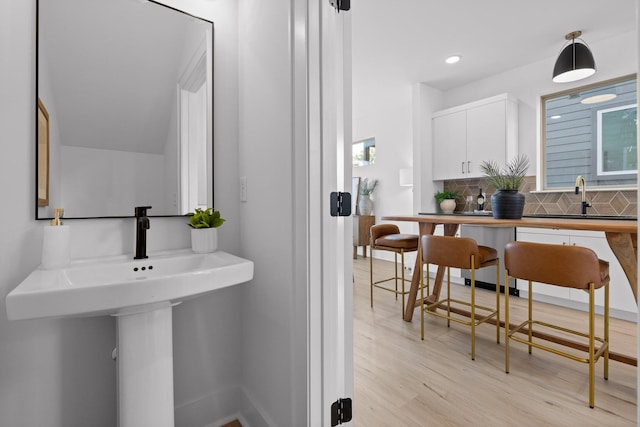 bathroom featuring recessed lighting, a sink, decorative backsplash, and wood finished floors