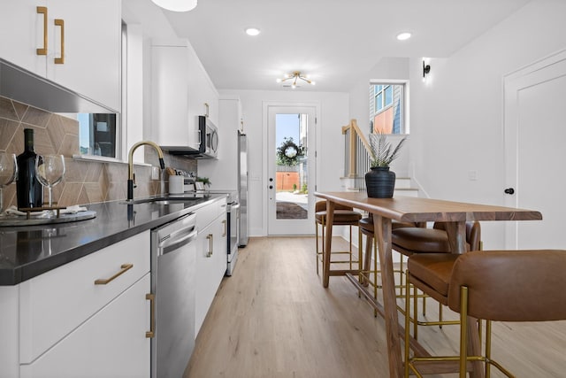 kitchen with a sink, white cabinetry, appliances with stainless steel finishes, tasteful backsplash, and dark countertops