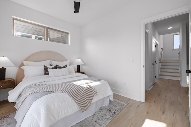 bedroom with light wood-style flooring, multiple windows, baseboards, and a ceiling fan