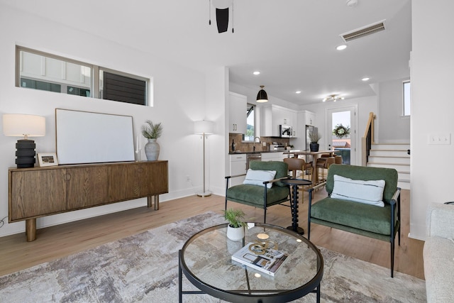 living room featuring recessed lighting, visible vents, light wood-style flooring, baseboards, and stairs