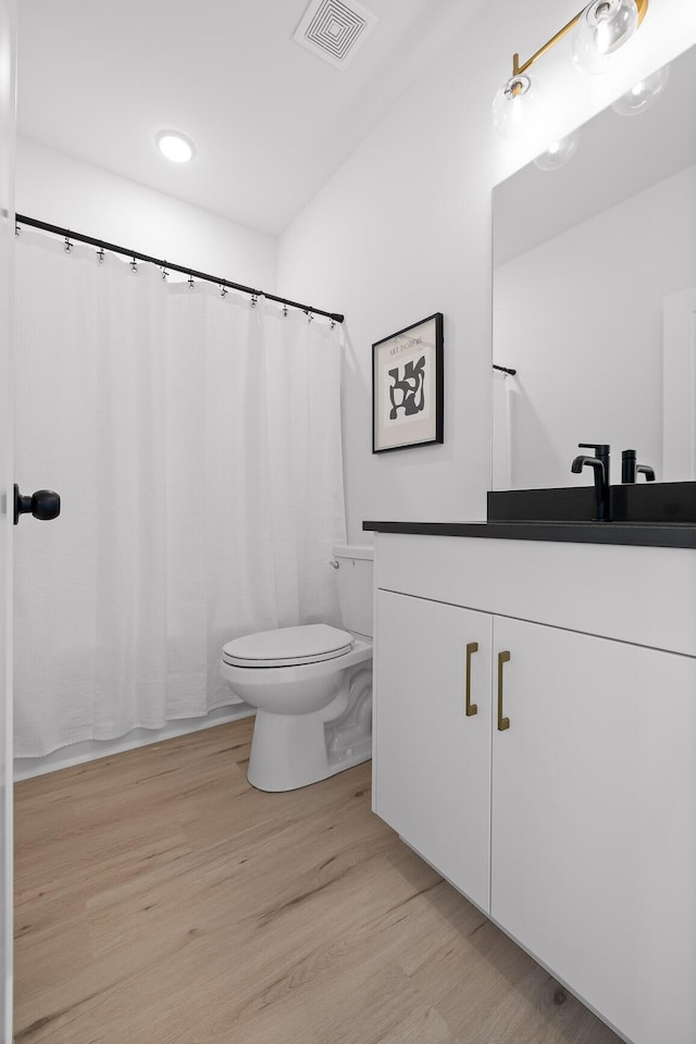 full bathroom with toilet, visible vents, wood finished floors, and vanity