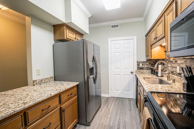 kitchen with brown cabinetry, stainless steel fridge, visible vents, and a sink