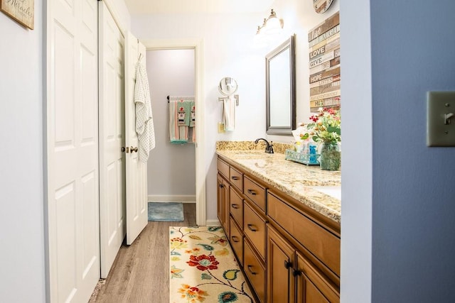 full bath featuring double vanity, wood finished floors, a sink, and baseboards