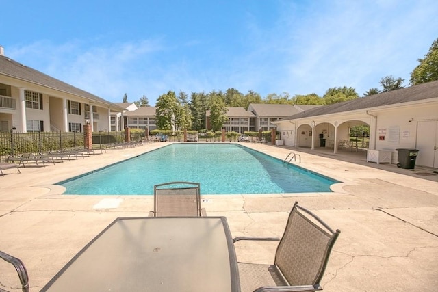 community pool with a patio, fence, and a residential view