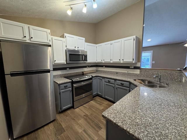 kitchen featuring dark wood finished floors, appliances with stainless steel finishes, a peninsula, white cabinetry, and a sink