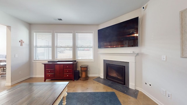 living area with a fireplace with flush hearth, visible vents, baseboards, and wood finished floors