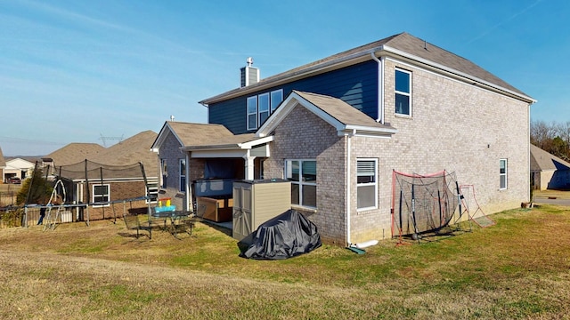 rear view of house with a trampoline, brick siding, a lawn, and a chimney