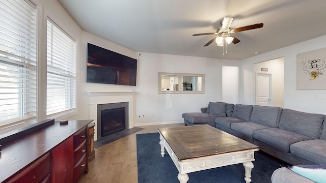 living area featuring light wood finished floors, a fireplace with flush hearth, a ceiling fan, and baseboards