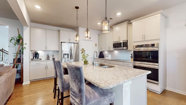 kitchen with light stone counters, a kitchen island with sink, stainless steel appliances, a sink, and hanging light fixtures