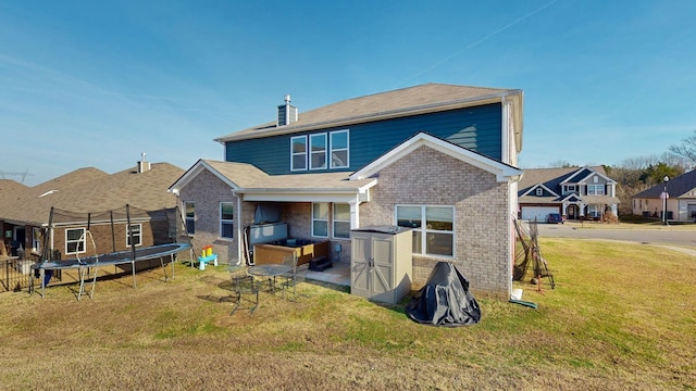 rear view of house featuring a trampoline, a residential view, brick siding, and a yard