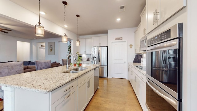 kitchen featuring visible vents, appliances with stainless steel finishes, a kitchen island with sink, white cabinets, and a sink