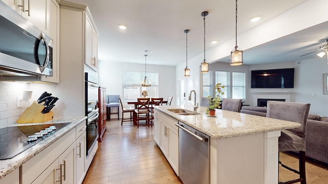 kitchen featuring open floor plan, a kitchen island with sink, stainless steel appliances, pendant lighting, and a sink