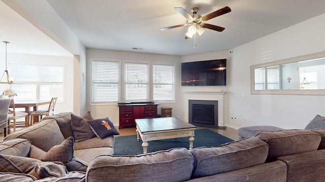 living area featuring a fireplace with flush hearth, a healthy amount of sunlight, and ceiling fan