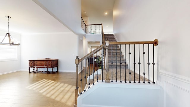 staircase with a notable chandelier, a high ceiling, wood finished floors, and baseboards