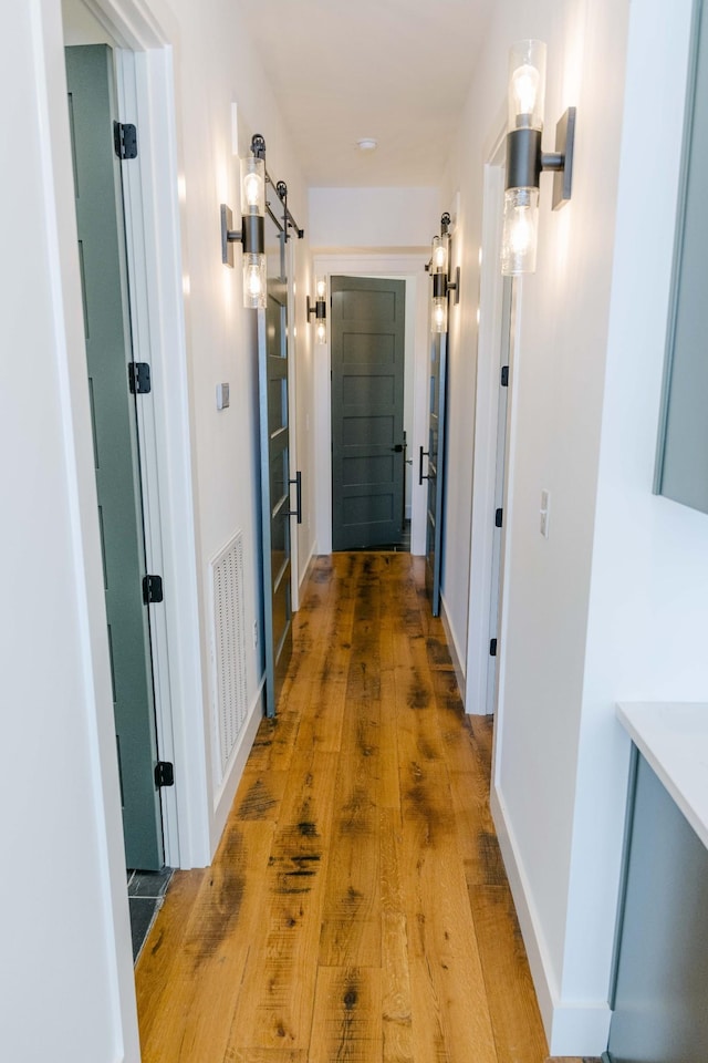 corridor with wood finished floors, visible vents, baseboards, and a barn door