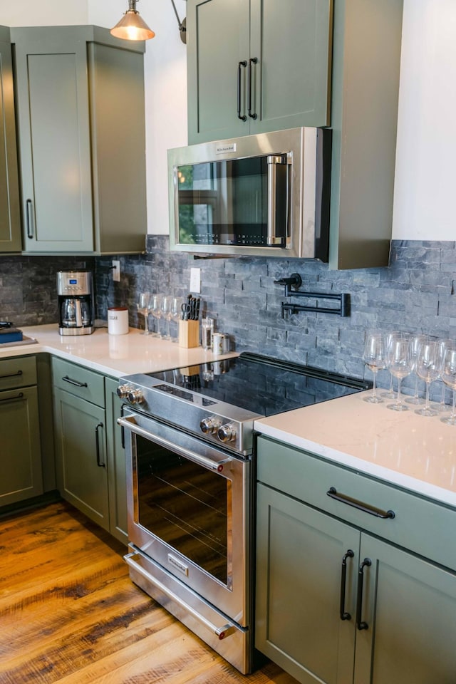 kitchen with green cabinets, appliances with stainless steel finishes, light wood finished floors, and decorative backsplash