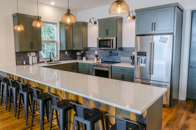 kitchen featuring premium appliances, a sink, a kitchen breakfast bar, light countertops, and hanging light fixtures