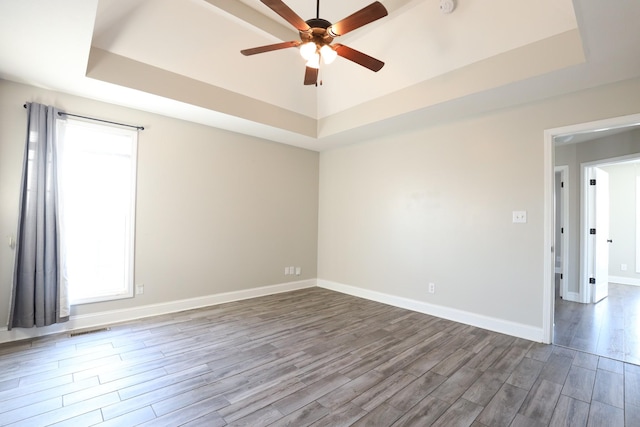 spare room with ceiling fan, wood finished floors, visible vents, baseboards, and a tray ceiling