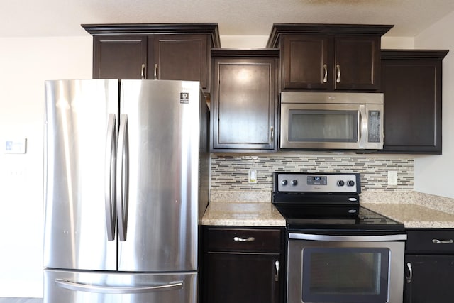 kitchen featuring dark brown cabinetry, appliances with stainless steel finishes, light stone counters, and backsplash