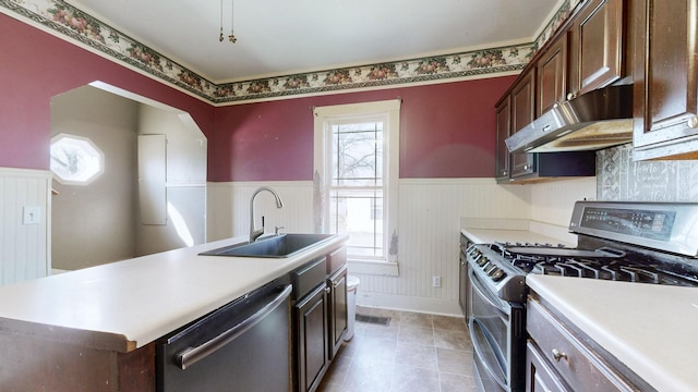 kitchen featuring stainless steel appliances, light countertops, wainscoting, a sink, and under cabinet range hood