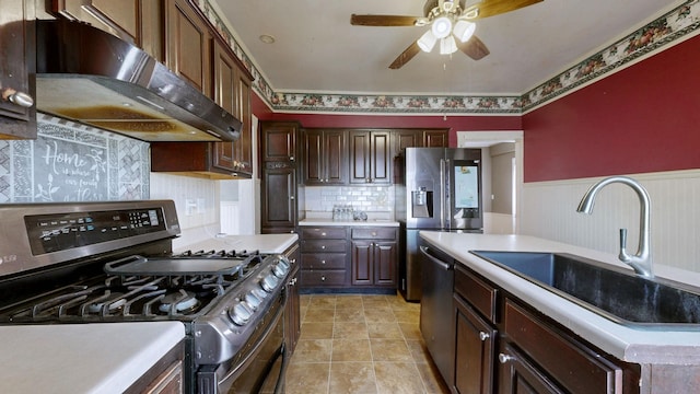 kitchen with stainless steel appliances, light countertops, wainscoting, a sink, and under cabinet range hood