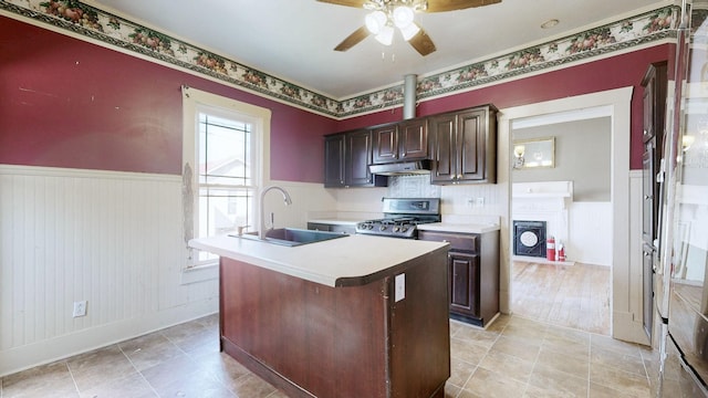 kitchen with under cabinet range hood, a wainscoted wall, a sink, light countertops, and range