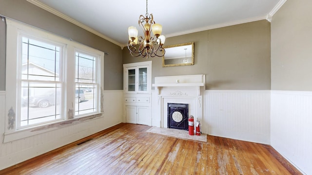 unfurnished living room featuring visible vents, wainscoting, a fireplace with flush hearth, hardwood / wood-style floors, and crown molding