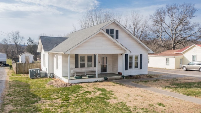 bungalow-style house with a shingled roof, covered porch, fence, central air condition unit, and a front yard