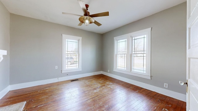 unfurnished room with baseboards, wood-type flooring, visible vents, and a healthy amount of sunlight