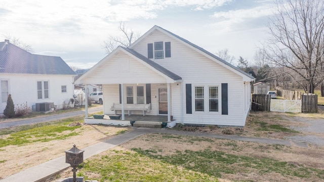 bungalow-style home featuring central air condition unit, covered porch, and fence