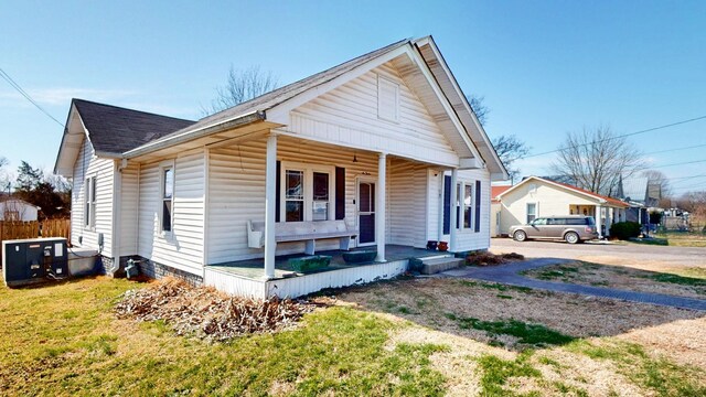 bungalow-style home with covered porch, a shingled roof, fence, and a front yard