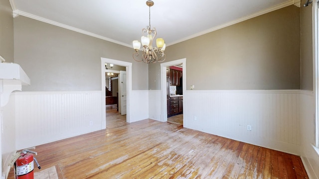 unfurnished room featuring a wainscoted wall, wood-type flooring, a chandelier, and crown molding