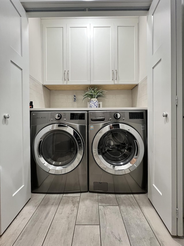 clothes washing area featuring wood tiled floor, cabinet space, and washing machine and clothes dryer