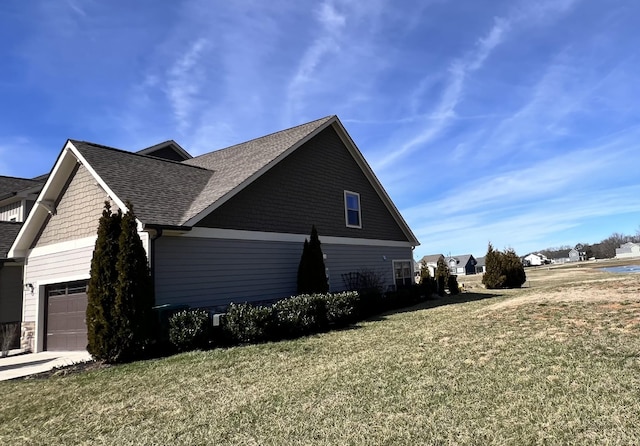 view of side of property with a garage, concrete driveway, a shingled roof, and a lawn