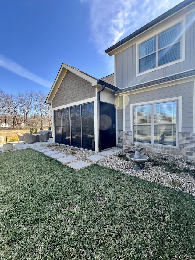 back of property featuring a patio, a sunroom, a yard, stone siding, and board and batten siding