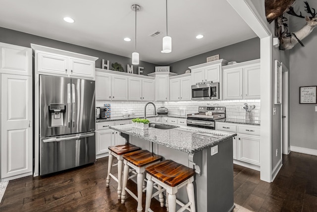 kitchen with a center island with sink, light stone countertops, stainless steel appliances, white cabinetry, and a sink