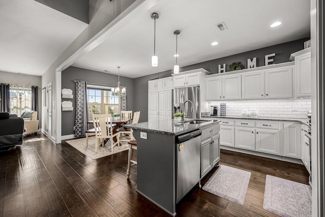 kitchen featuring stainless steel appliances, dark stone countertops, a center island with sink, and white cabinetry