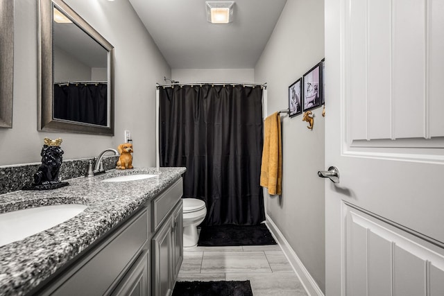 full bath featuring double vanity, baseboards, toilet, curtained shower, and a sink